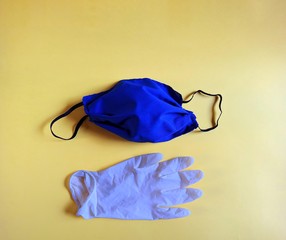 Blue handmade medical mask and white latex glove on yellow background. medical concept