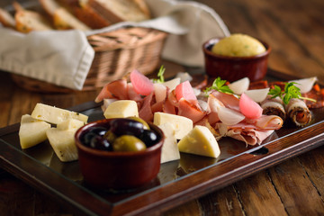 Obraz na płótnie Canvas Italian antipasto platter on a glass plate with cheese, ham, olives, chorizo and bread in the background