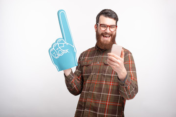 Photo of cheerful smiling young man looking at smartphone and holding fan foam glove