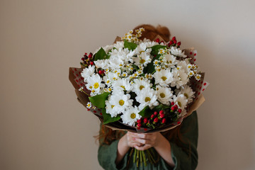The girl covers her face with a large bouquet of flowers