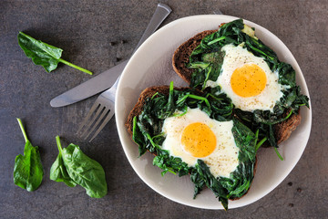 Healthy toasts with spinach and egg on a plate. Above view over a dark stone background.