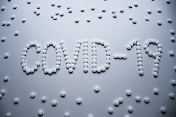 Text phrase Covid-19 sign concept made from white pills on a white background