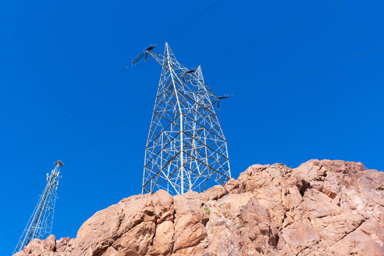 High voltage transmission towers with parallel lines on the top of the rocky hill in the blue sky