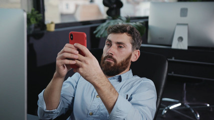 Joyful caucasian office employee laughing browsing fun content on smartphone relaxing during break in company office. Office people. Fun activity.