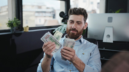 Cheerful smiling young man business manager counting bundle of money dollars celebrating profits...