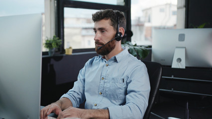 Customer service manager keyboarding on desktop computer consulting a client on phone call working in company office.