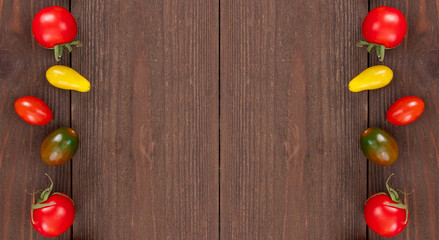 Red, green, yellow cherry tomatoes on rustic wooden surface with copy space. Frame of fresh vegetables, top view