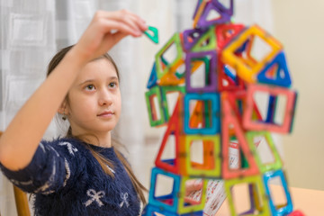 little girl playing colorful magnet plastic blocks kit at indoor playground. girl made a toy robot. The child playing educational games. Early childhood development