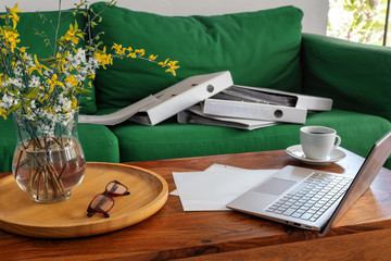 Home office in the living room, laptop on the coffee table and ring binders on the couch,...