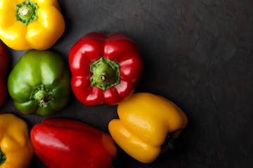 Red, yellow and green peppers against a dark grey background.  A landscape flat lay view of an assortment of peppers.  Ideal dark background with space for text.