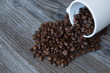 Coffee beans fall out of a cup on a wooden table.