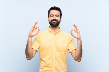 Young man with beard over isolated blue background in zen pose