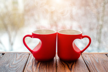 two heart shaped mugs with tea on the background of a window in winter