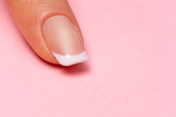 single female finger with a beautiful manicure on a pink background, close-up. clean healthy fingernails. copy space. place for text and logo.