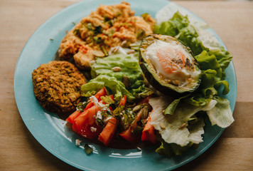 delicious healthy breakfast: baked avocado with chicken egg, toasts with whole grain bread and homemade hummus with lime juice, falafel, tomato slices with feta, parsley, dill and coriander, iceberg 
