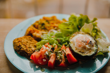 delicious healthy breakfast: baked avocado with chicken egg, toasts with whole grain bread and homemade hummus with lime juice, falafel, tomato slices with feta, parsley, dill and coriander, iceberg 