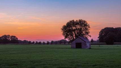 Sunset at a Dutch farm landscape near the village of Zenderen. It lies in the region of Twente (in the province Overijssel in the eastern Netherlands ). A lonely shed with graffiti can be seen.