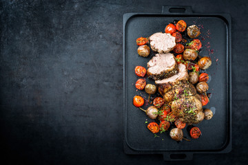 Traditional barbecue rolled lamb roast sliced with tomatoes and mini eggplant as top view on a...