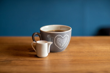 a cup of coffee is on a wooden table with a cup of milk. blue background. Front view