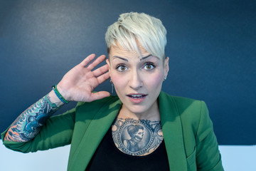 ragazza bionda tatuata con giacca verde si mette la mano all'orecchio perchè non sente
