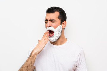 Man shaving his beard over isolated white background yawning and covering wide open mouth with hand