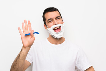 Man shaving his beard over isolated white background saluting with hand with happy expression