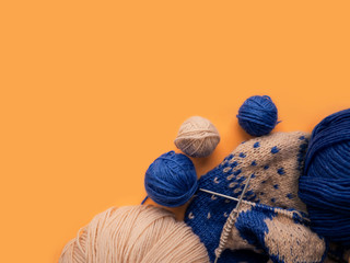 Knitting on needles. Top view of blue and beige yarn balls on an orange background. Hobby