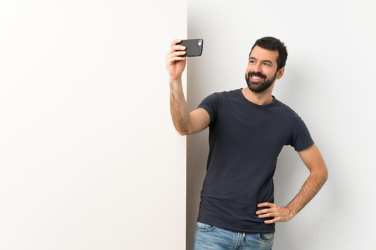 Young handsome man with beard holding a big empty placard making a selfie
