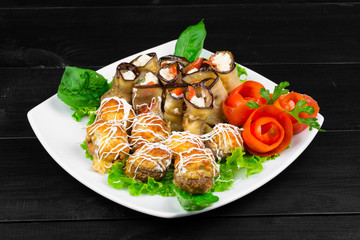 fishballs and meatballs with eggplant rolls with cottage cheese and tomato, parsley on a white plate on a black background