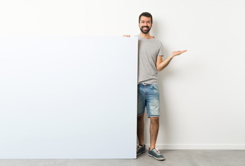 Young handsome man with beard holding a big blue empty placard holding copyspace imaginary on the...
