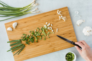 A top down view of green onion being chopped up on a wooden cutting board.