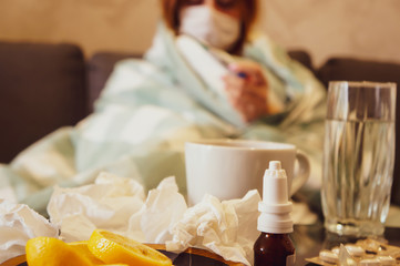 The concept of the common cold or seasonal flu. A young girl in a mask looks at a thermometer...
