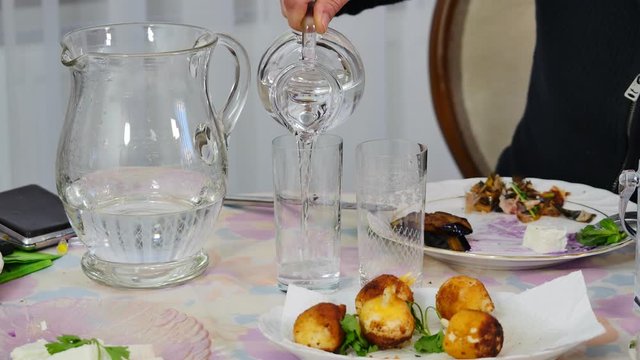 Woman adds water into RAKI and cheers. It is often served in flat cylindrical glasses with meze. Raki is absolutely clear but when you mix it with ice or water for drinking it turns into milky white