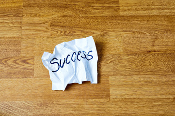 Crumpled papers with the word succes on wooden background.
