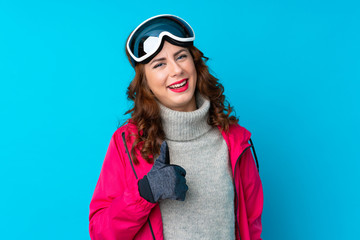 Skier woman with snowboarding glasses over isolated blue wall giving a thumbs up gesture