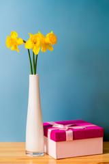Bouquet of yellow daffodils in a vase next to a gift box