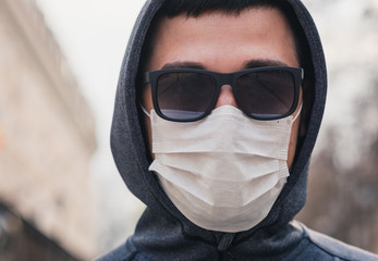 A man in a medical mask on the street. The head of a man in a hood and black glasses on the street. Quarantine. Pandemic. Coronavirus. Vaccines. Covid-19