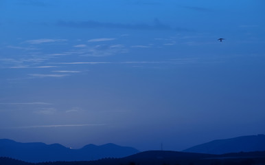 Dark blue sky at dusk with the silhouette of a distant hang glider and mountains in the background