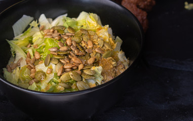 Chopped lettuce salad and seeds in black bowl