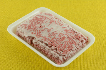 Raw frozen hamburger meat in polystyrene butcher packaging on table