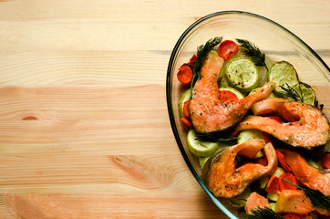 Baked salmon with vegetables: zucchini, zucchini, carrots, onions garnished with sprigs of dill in a glass tray