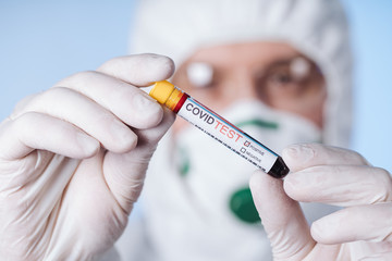 Microbiologist with a tube of biological sample contaminated by Coronavirus with label Covid Test....