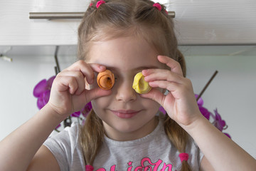 Little girl sitting on kitchen and putting dumplings on her eyes. Coronavirus quarantine concept. Stay at home.