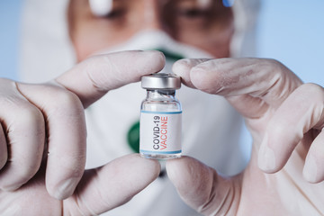 Glass medical bottle in a doctor's hand. A bottle with a cure holds a palm in silicone gloves in a...