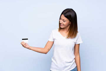 Naklejka premium Young woman over isolated blue background holding a credit card