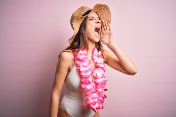Young beautiful brunette woman on vacation wearing swimsuit and Hawaiian flowers lei shouting and screaming loud to side with hand on mouth. Communication concept.