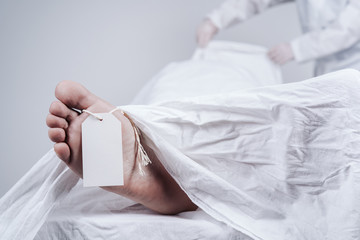 Feet of a dead body, with an identification tag - blank sign attached to a big toe. Covered with a...