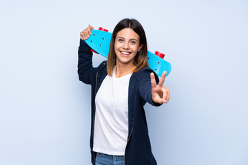 Young woman over isolated blue background with skate and making victory gesture