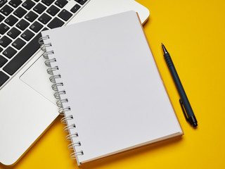 Workplace - laptop, notebook and pen for remote work on a yellow background table. Freelance...