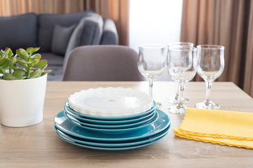 Clean dishes on the table. Stacked clean blue and white plates, glasses and yellow napkins on wooden table in the kitchen. Succulent plant